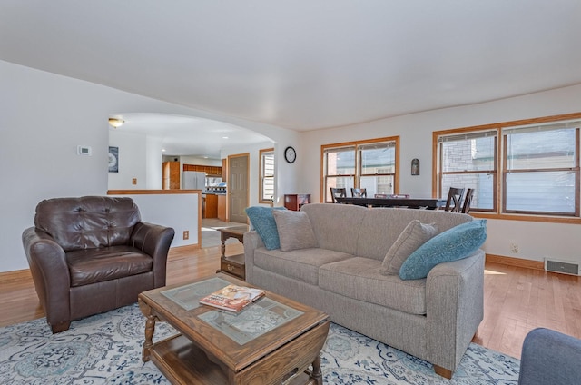 living area featuring visible vents, baseboards, light wood-type flooring, and arched walkways