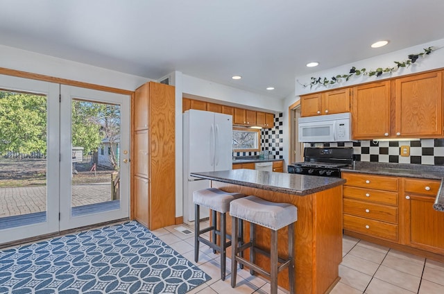 kitchen with dark countertops, white appliances, backsplash, a kitchen island, and light tile patterned flooring