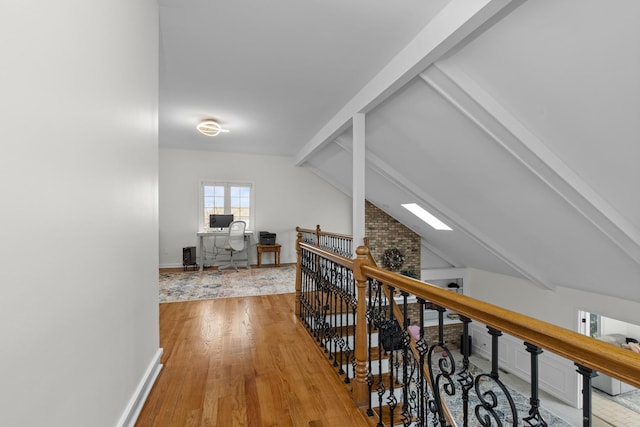corridor featuring an upstairs landing, baseboards, wood finished floors, and lofted ceiling with skylight