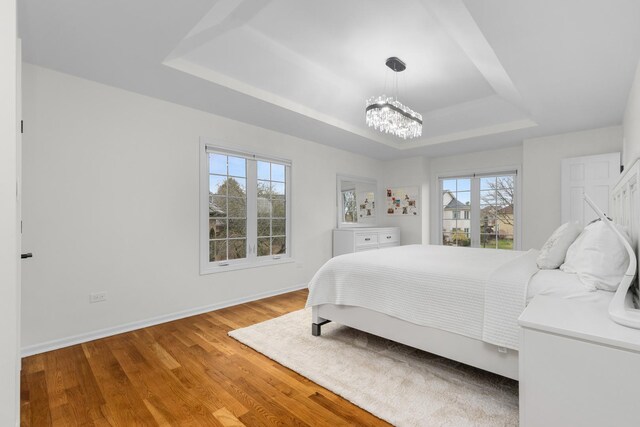bedroom with a tray ceiling, wood finished floors, a notable chandelier, and baseboards