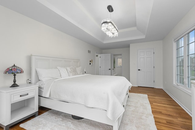 bedroom featuring a raised ceiling, a chandelier, wood finished floors, and baseboards