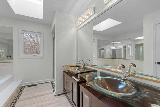 bathroom featuring a sink, a skylight, double vanity, and baseboards