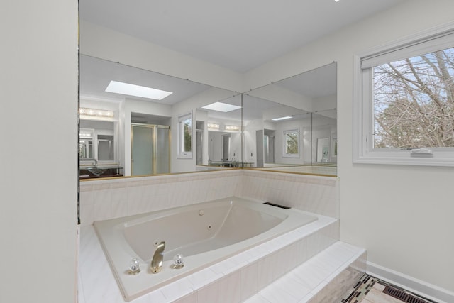 bathroom with a jetted tub, a skylight, baseboards, a shower stall, and a healthy amount of sunlight