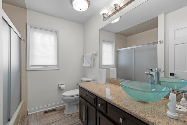 full bath featuring vanity, visible vents, toilet, combined bath / shower with glass door, and baseboards