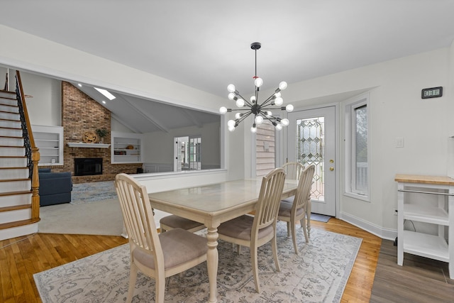 dining area featuring stairway, a notable chandelier, a brick fireplace, and wood finished floors