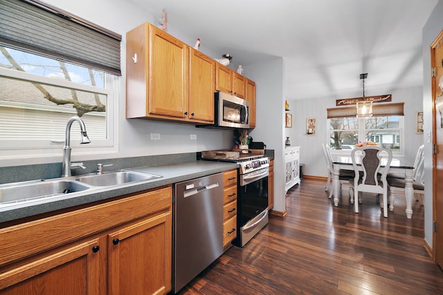 kitchen featuring hanging light fixtures, a sink, dark countertops, dark wood-style floors, and stainless steel appliances