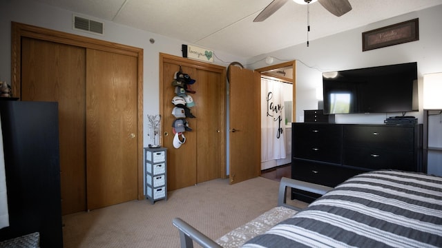 bedroom with visible vents, carpet flooring, a ceiling fan, and two closets
