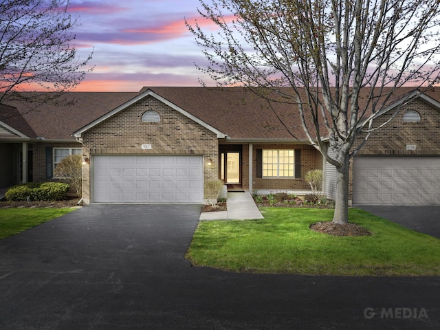 view of front of property with a garage, aphalt driveway, a lawn, brick siding, and roof with shingles