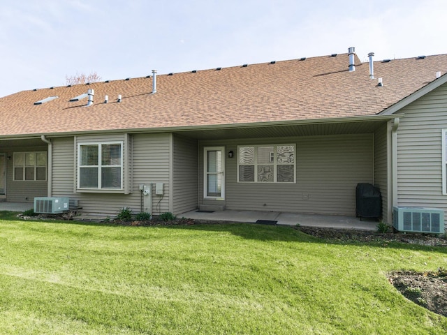 rear view of property with cooling unit, roof with shingles, a patio area, and a yard