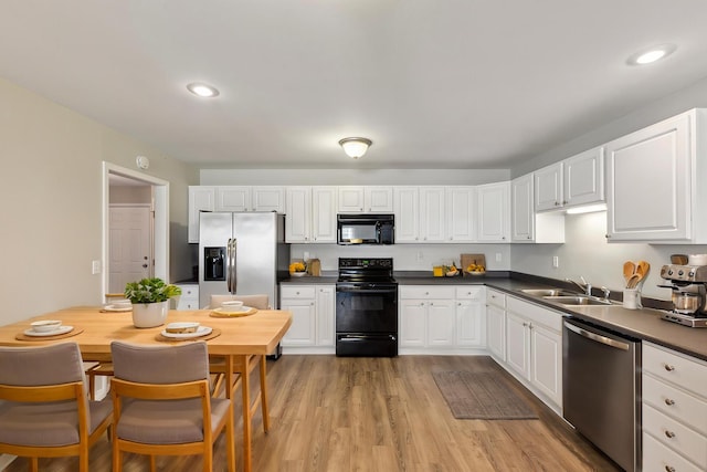 kitchen featuring white cabinets, black appliances, dark countertops, and a sink