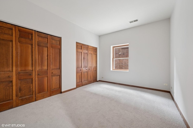 unfurnished bedroom featuring light carpet, baseboards, and two closets