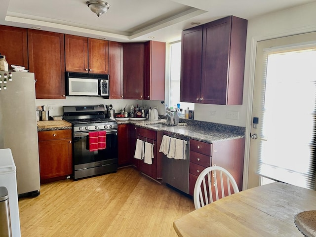 kitchen featuring a raised ceiling, reddish brown cabinets, a sink, light wood-type flooring, and appliances with stainless steel finishes