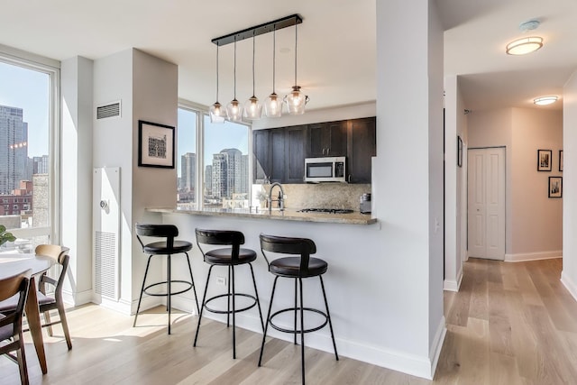 kitchen with a kitchen breakfast bar, light wood-style flooring, a view of city, stainless steel microwave, and visible vents