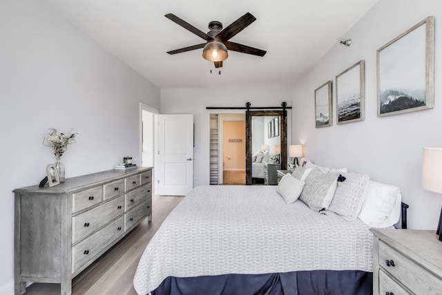 bedroom with a barn door, ceiling fan, and wood finished floors