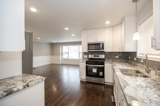 kitchen with white cabinets, a sink, appliances with stainless steel finishes, wainscoting, and light stone counters