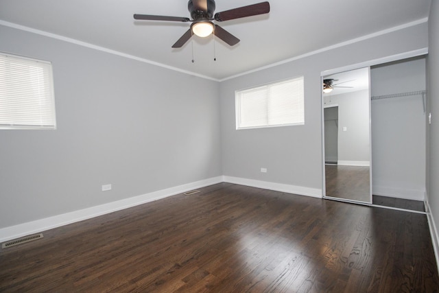 unfurnished bedroom featuring dark wood-style flooring, a closet, baseboards, ornamental molding, and visible vents