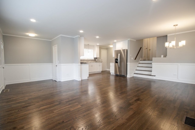 unfurnished living room with crown molding, visible vents, stairway, dark wood-style flooring, and a notable chandelier