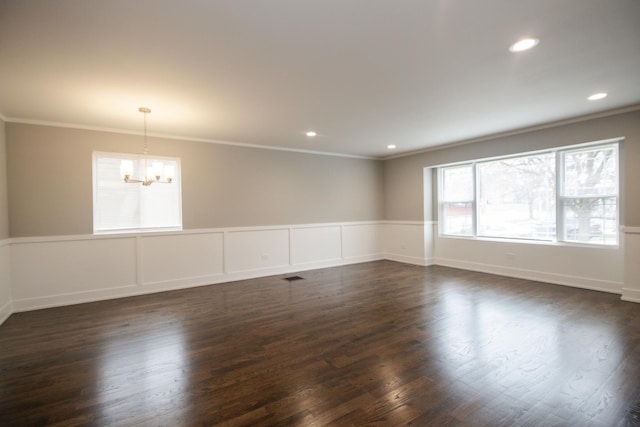 unfurnished room featuring visible vents, an inviting chandelier, ornamental molding, dark wood-type flooring, and a wainscoted wall