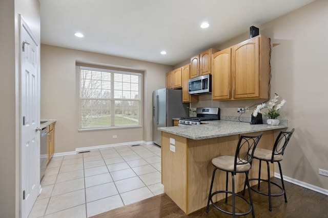 kitchen with appliances with stainless steel finishes, a breakfast bar area, a peninsula, and baseboards