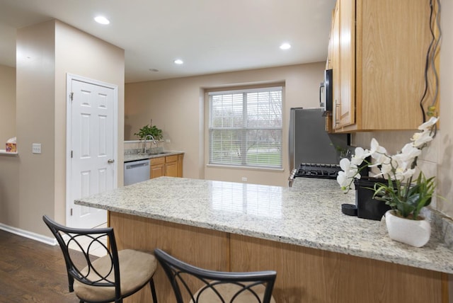 kitchen featuring dark wood-style floors, light stone countertops, a breakfast bar area, a peninsula, and appliances with stainless steel finishes