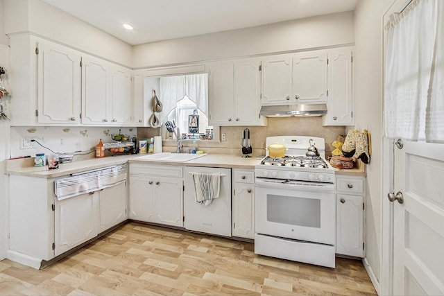 kitchen featuring white appliances, light countertops, white cabinetry, wall chimney exhaust hood, and a sink