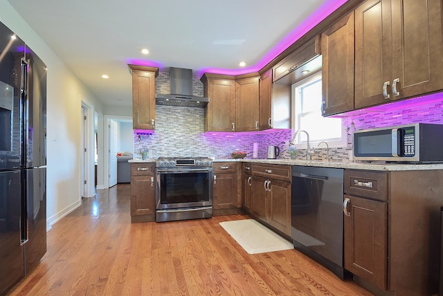 kitchen with wall chimney range hood, appliances with stainless steel finishes, decorative backsplash, and a sink