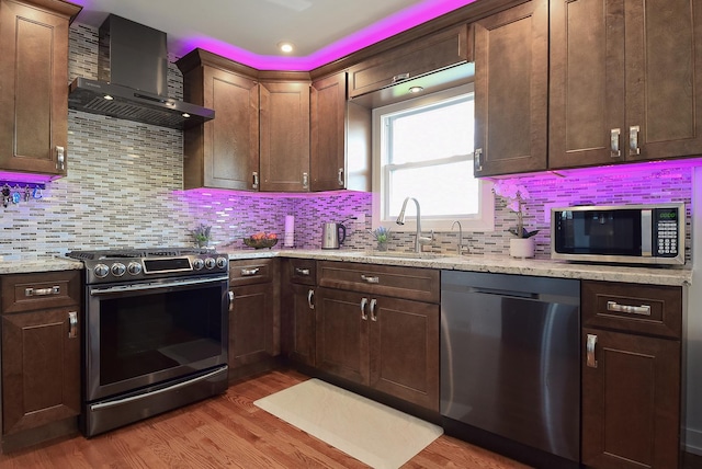 kitchen featuring a sink, stainless steel appliances, light wood finished floors, and wall chimney exhaust hood