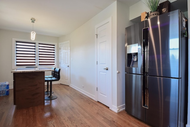 kitchen with stainless steel fridge with ice dispenser, a kitchen breakfast bar, decorative light fixtures, baseboards, and wood finished floors