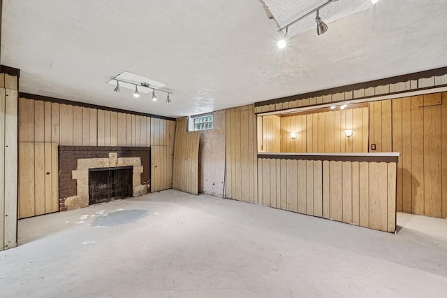 unfurnished living room with concrete floors, track lighting, a brick fireplace, and wood walls