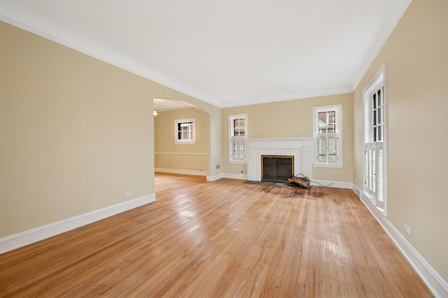 unfurnished living room featuring arched walkways, light wood-style flooring, baseboards, and a wealth of natural light