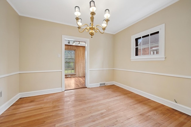 unfurnished room with an inviting chandelier, wood finished floors, visible vents, crown molding, and baseboards