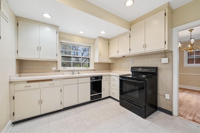 kitchen featuring an inviting chandelier, light countertops, backsplash, black range with electric stovetop, and a sink