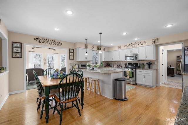 kitchen with stainless steel appliances, tasteful backsplash, light wood-style flooring, and pendant lighting