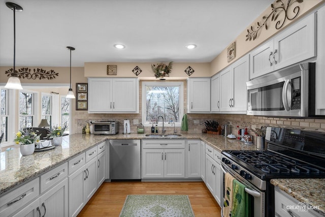kitchen with light wood-type flooring, appliances with stainless steel finishes, a sink, and backsplash