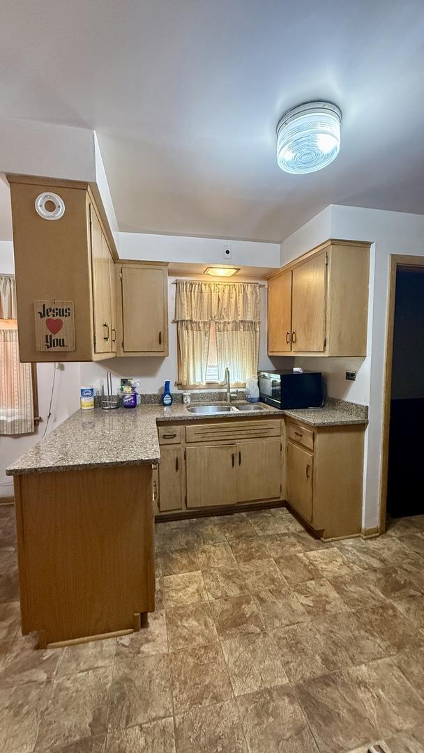 12450 S Yale Ave, Chicago, IL 60628 - kitchen with a sink, light countertops, stone finish floor, a peninsula, and black microwave