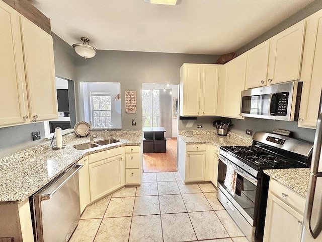 kitchen featuring a peninsula, a sink, light stone countertops, and stainless steel appliances