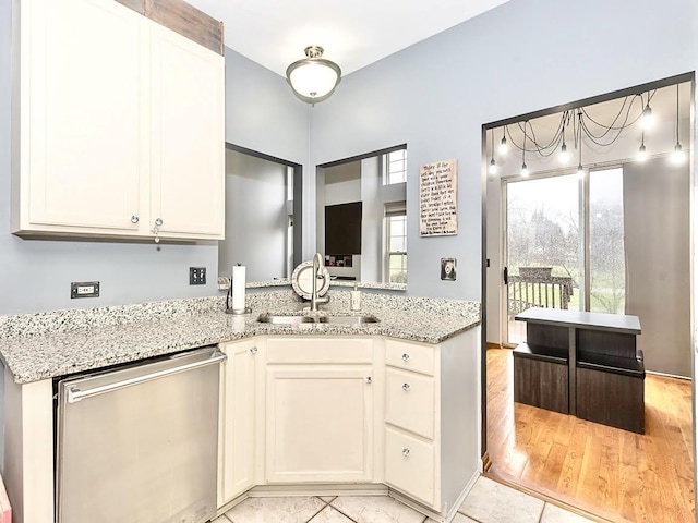 kitchen featuring stainless steel dishwasher, a peninsula, white cabinets, light stone counters, and a sink