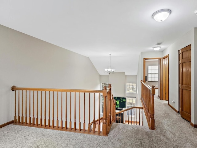 hall with a chandelier, an upstairs landing, baseboards, and carpet floors