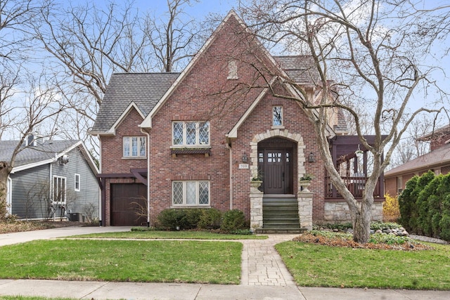 tudor house with a front lawn, driveway, brick siding, and central air condition unit