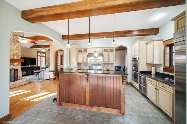 kitchen with cream cabinets, arched walkways, dark countertops, and stainless steel appliances