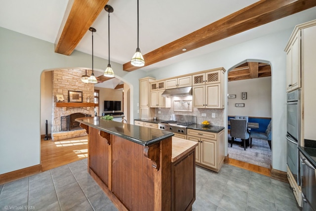 kitchen featuring cream cabinetry, arched walkways, and under cabinet range hood