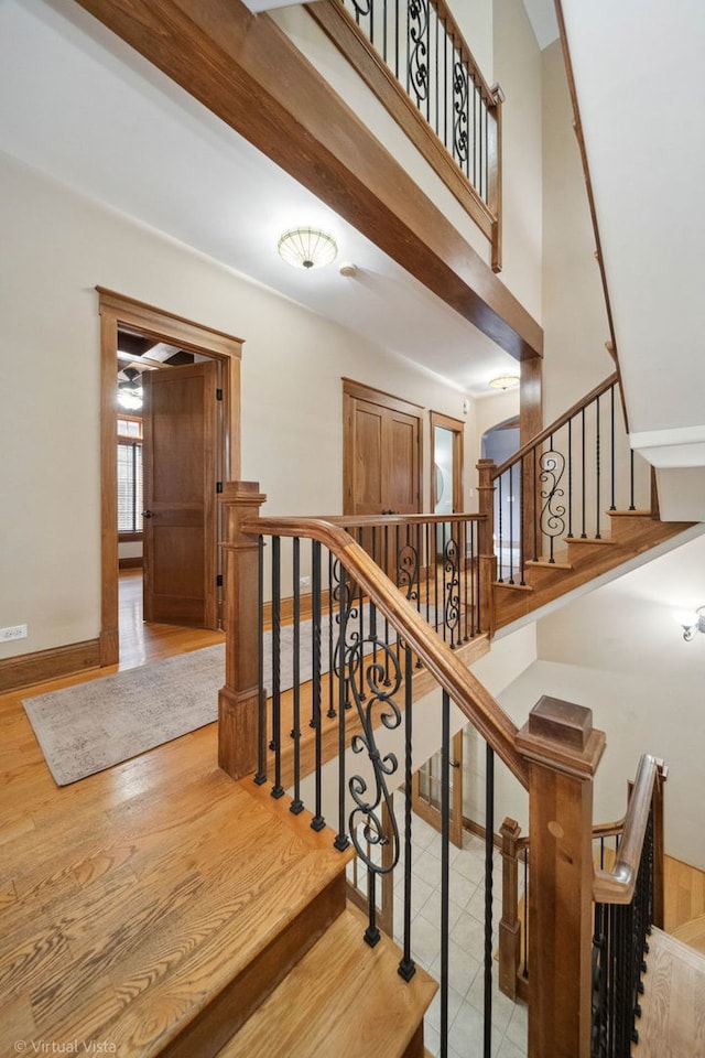 stairway featuring baseboards, wood finished floors, and a towering ceiling