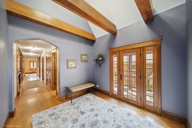 doorway to outside featuring visible vents, arched walkways, light wood-type flooring, baseboards, and lofted ceiling with beams