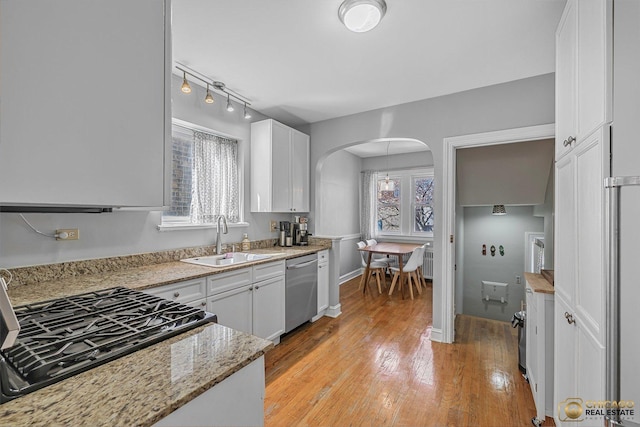 kitchen featuring a sink, light wood-type flooring, dishwasher, arched walkways, and white cabinetry