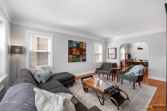 living area featuring baseboards, wood finished floors, arched walkways, and ornamental molding