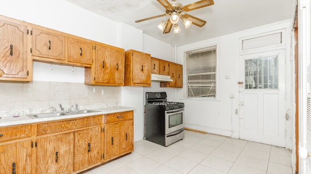 kitchen with a sink, light countertops, a ceiling fan, under cabinet range hood, and stainless steel gas range oven