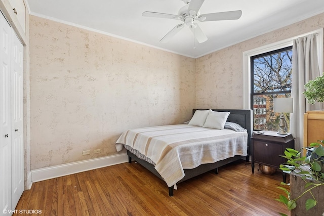 bedroom with wallpapered walls, wood finished floors, ornamental molding, a closet, and baseboards