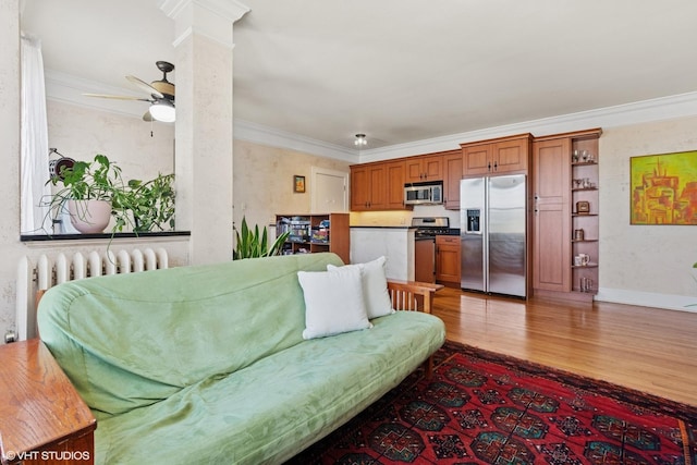 living room with radiator, wood finished floors, a ceiling fan, crown molding, and decorative columns