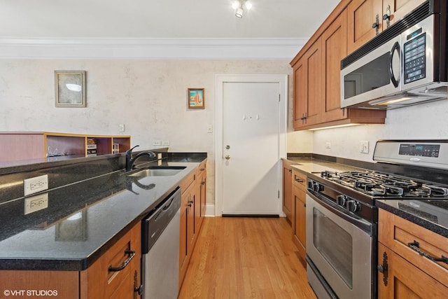 kitchen with brown cabinets, stainless steel appliances, ornamental molding, a sink, and light wood-style floors