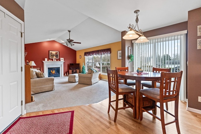 dining space with light wood-type flooring, lofted ceiling, a glass covered fireplace, and ceiling fan